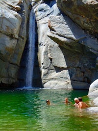 two people swimming in the water near a waterfall