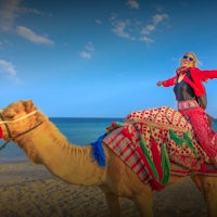 a woman riding a camel on the beach