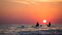 two people paddling in the ocean at sunset